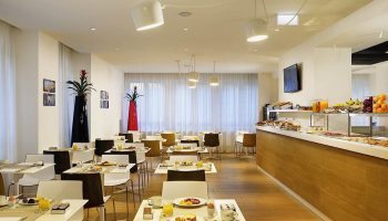 UNAHOTELS Century Milano breakfast area. Gay-friendly hotel with buffet, tables set with juice, coffee, and pastries. Modern, bright interior.