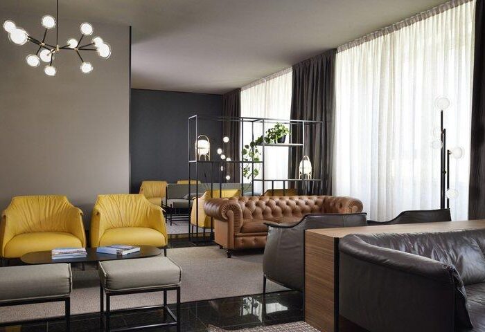 UNAHOTELS Century Milano gay-friendly hotel lobby. Stylish seating area with yellow armchairs and leather sofas, modern lighting.