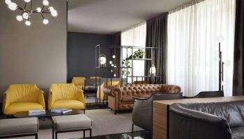 UNAHOTELS Century Milano gay-friendly hotel lobby. Stylish seating area with yellow armchairs and leather sofas, modern lighting.