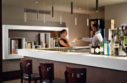 UNAHOTELS Century Milano bar: Bartender serves a cocktail to a guest. Gay-friendly hotel with stylish interior, ideal for gay men travelers.
