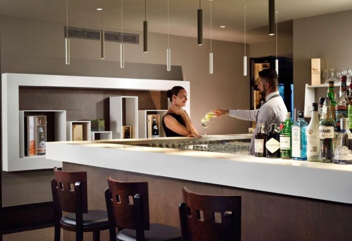 UNAHOTELS Century Milano bar: Bartender serves a cocktail to a guest. Gay-friendly hotel with stylish interior, ideal for gay men travelers.
