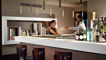 UNAHOTELS Century Milano bar: Bartender serves a cocktail to a guest. Gay-friendly hotel with stylish interior, ideal for gay men travelers.