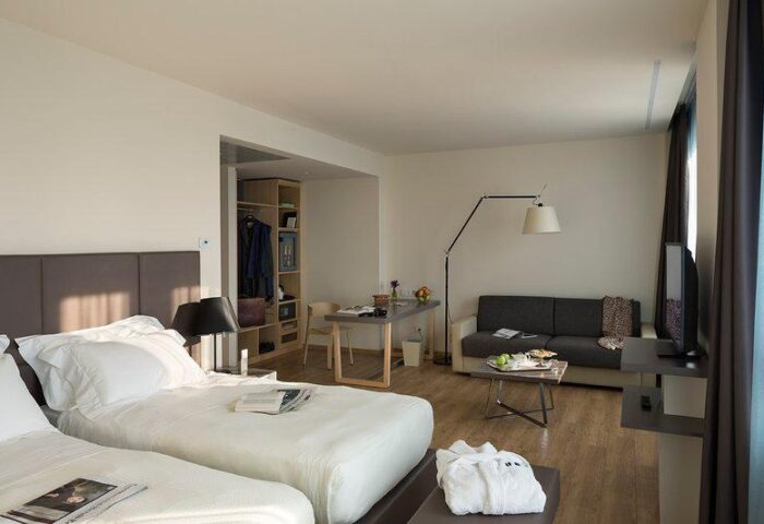 UNAHOTELS Century Milano gay-friendly hotel room. Two beds, sofa, desk, and closet. Modern design for gay men's travel in Milan, Italy.