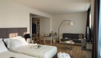UNAHOTELS Century Milano gay-friendly hotel room. Two beds, sofa, desk, and closet. Modern design for gay men's travel in Milan, Italy.