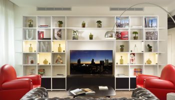 UNAHOTELS Century Milano gay-friendly hotel room. Living area with TV, couch, bookshelves, and red chairs. Modern design in Milan, Italy.