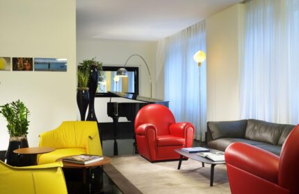 UNAHOTELS Century Milano lounge area. Gay-friendly hotel with piano, colorful armchairs, and modern design. Ideal for gay men travelers.