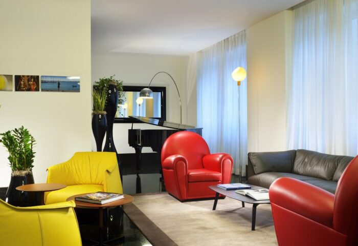 UNAHOTELS Century Milano lounge area. Gay-friendly hotel with piano, colorful armchairs, and modern design. Ideal for gay men travelers.