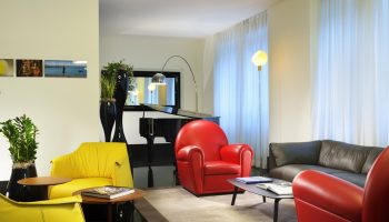 UNAHOTELS Century Milano lounge area. Gay-friendly hotel with piano, colorful armchairs, and modern design. Ideal for gay men travelers.