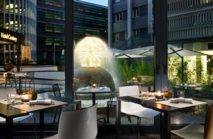 UNAHOTELS Century Milano gay-friendly hotel dining. Tables set near a water fountain. Milan hotel for gay travelers.