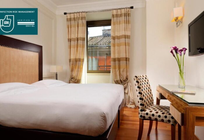 UNAHOTELS Decò Roma gay-friendly room. Pet-friendly hotel with double bed, desk, chair, and window. UNA Safe infection risk management verified.