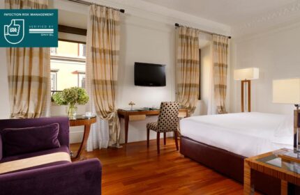 UNAHOTELS Decò Roma gay-friendly room. Pet-friendly hotel room with desk, TV, chair, bed, and purple sofa. Elegant interior design.