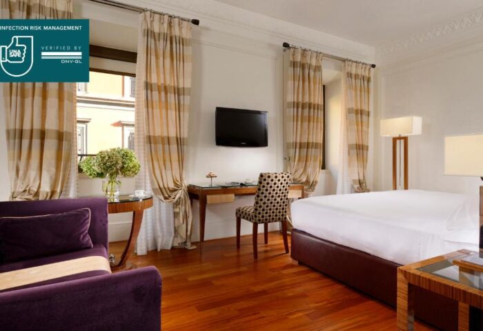 UNAHOTELS Decò Roma gay-friendly room. Pet-friendly hotel room with desk, TV, chair, bed, and purple sofa. Elegant interior design.