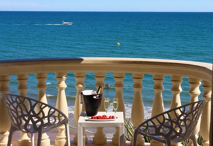 URH Sitges Playa gay-friendly hotel balcony view. Champagne, strawberries, and chairs overlook the beach. Pet-friendly hotel option.