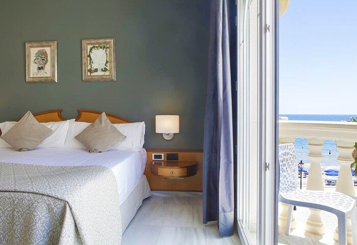 URH Sitges Playa gay-friendly hotel room with balcony view. Pet-friendly option. Bedroom interior with sea view. Travel advice for gay men.