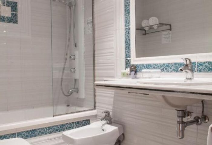 Bathroom at URH Sitges Playa, a gay-friendly, pet-friendly hotel. Features a shower, bidet, sink, and toilet. Tiled in white with blue accents.