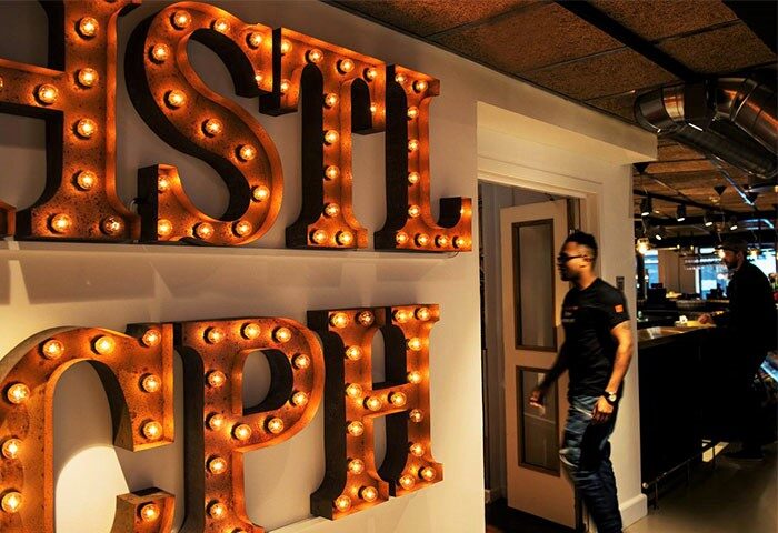 Urban House Copenhagen by MEININGER. Gay-friendly hotel's interior with illuminated letters spelling Hostel CPH. Man entering doorway.