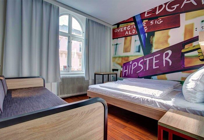 Urban House Copenhagen by MEININGER room. Gay-friendly hotel room with twin beds, hardwood floors, and a window with curtains. Hipster wall art.