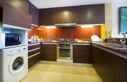 Urbana Sathorn Bangkok gay-friendly hotel kitchen. Modern design with wood cabinets, oven, microwave, washing machine, and sink. Bangkok travel.