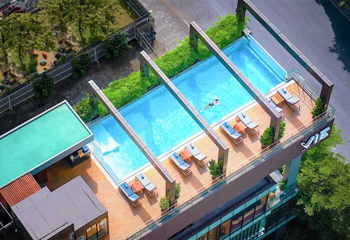 Rooftop pool at VIE Hotel Bangkok - MGallery, a gay-friendly hotel. Swimmer, deck chairs, and lush greenery. Perfect for gay travel in Thailand.