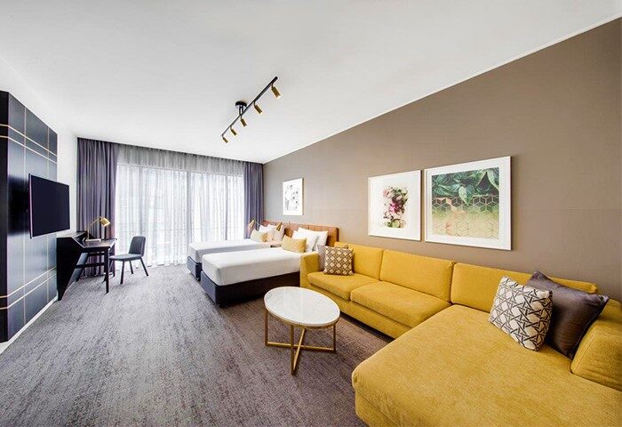 Vibe Hotel Sydney room with twin beds, yellow sofa, desk and TV. Gay-friendly hotel for gay men travelers in Sydney, Australia.