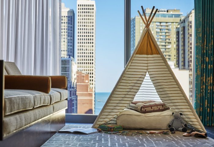 Viceroy Chicago gay-friendly hotel room. A child's teepee tent sits by a window with a city view. Sofa, toys, and a book are nearby.