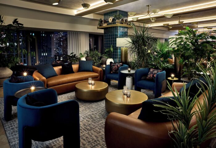 Viceroy Chicago, a gay-friendly hotel. Stylish lounge area with leather sofas, blue armchairs, and lush greenery. Nighttime city view.