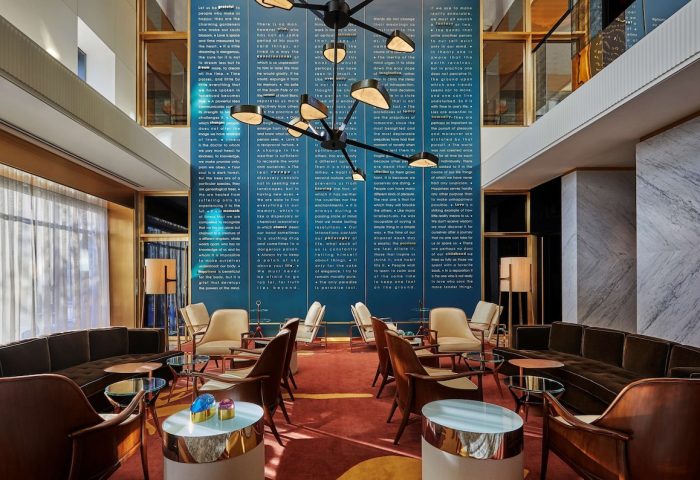 Viceroy Chicago gay-friendly hotel lounge area. Modern interior design with stylish seating, a unique light fixture, and a wall of text art.