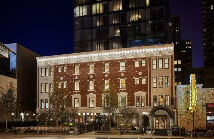 Viceroy Chicago hotel exterior at night. Gay-friendly hotel with vintage brick facade and modern tower. Outdoor seating area. Chicago travel.