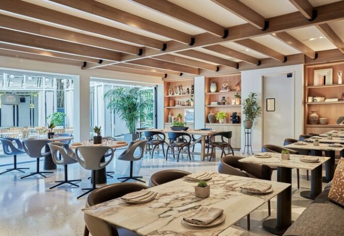 Viceroy Santa Monica gay-friendly hotel restaurant. Stylish dining area with marble tables, modern chairs, wood accents, and plants. Upscale ambiance.