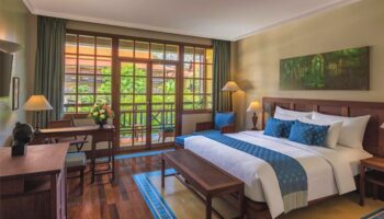 Victoria Angkor Resort & Spa gay-friendly hotel room. Balcony view, wooden furniture, king bed with blue accents. Luxury gay travel.