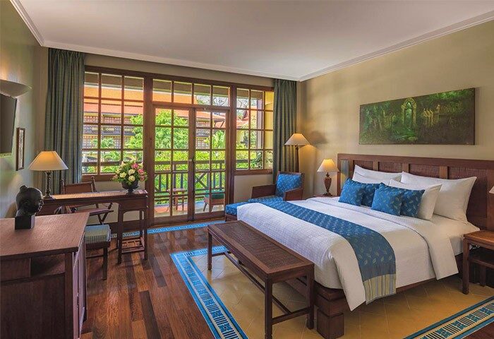 Victoria Angkor Resort & Spa gay-friendly hotel room. Balcony view, wooden furniture, king bed with blue accents. Luxury gay travel.