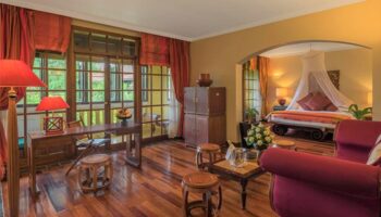 Victoria Angkor Resort & Spa gay-friendly hotel room. Suite interior with wooden floors, desk, and bedroom with canopy bed. Luxury gay travel.