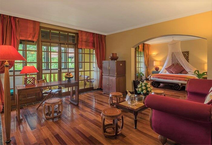 Victoria Angkor Resort & Spa gay-friendly hotel room. Suite interior with wooden floors, desk, and bedroom with canopy bed. Luxury gay travel.