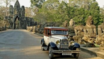Classic car at Victoria Angkor Resort & Spa, a gay-friendly hotel. Ancient temple gate and stone statues line the road in Siem Reap, Cambodia.