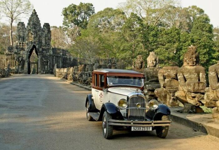 Classic car at Victoria Angkor Resort & Spa, a gay-friendly hotel. Ancient temple gate and stone statues line the road in Siem Reap, Cambodia.
