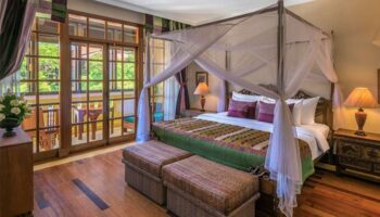 Victoria Angkor Resort & Spa gay-friendly hotel room with a four-poster bed, balcony, wooden floor, and warm lighting, ideal for gay men travelers.