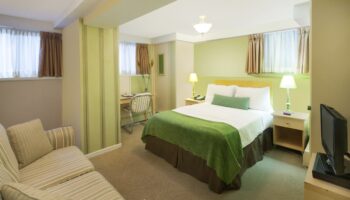 Victoria's Mansion Guest House room. Gay-friendly hotel bedroom with queen bed, desk, and striped sofa. Comfortable travel lodging.