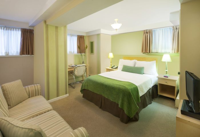Victoria's Mansion Guest House room. Gay-friendly hotel bedroom with queen bed, desk, and striped sofa. Comfortable travel lodging.