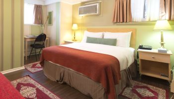 Victoria's Mansion Guest House room. Gay-friendly hotel featuring a bed with red blanket, desk, and nightstand. Comfortable travel lodging.