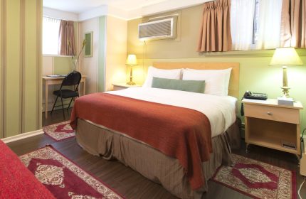 Victoria's Mansion Guest House room. Gay-friendly hotel featuring a bed with red blanket, desk, and nightstand. Comfortable travel lodging.