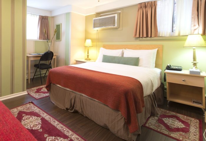 Victoria's Mansion Guest House room. Gay-friendly hotel featuring a bed with red blanket, desk, and nightstand. Comfortable travel lodging.