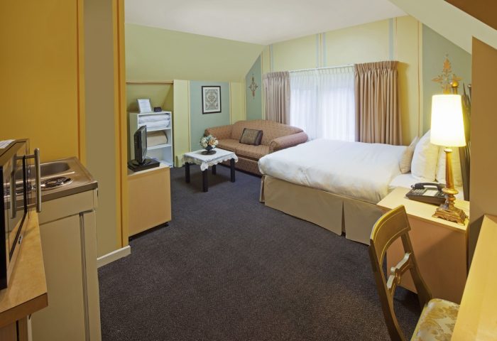 Victoria's Mansion Guest House room. Gay-friendly hotel with bed, sofa, kitchenette, desk, and chair. A cozy space for gay travelers.