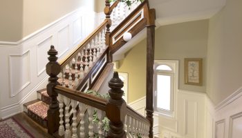 Staircase at Victoria's Mansion Guest House, a gay-friendly hotel. Ornate wood banister, carpeted steps, and elegant decor. Gay travel lodging.