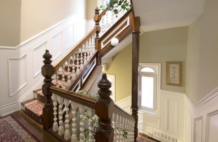 Staircase at Victoria's Mansion Guest House, a gay-friendly hotel. Ornate wood banister, carpeted steps, and elegant decor. Gay travel lodging.