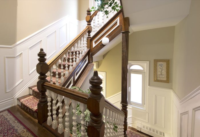 Staircase at Victoria's Mansion Guest House, a gay-friendly hotel. Ornate wood banister, carpeted steps, and elegant decor. Gay travel lodging.