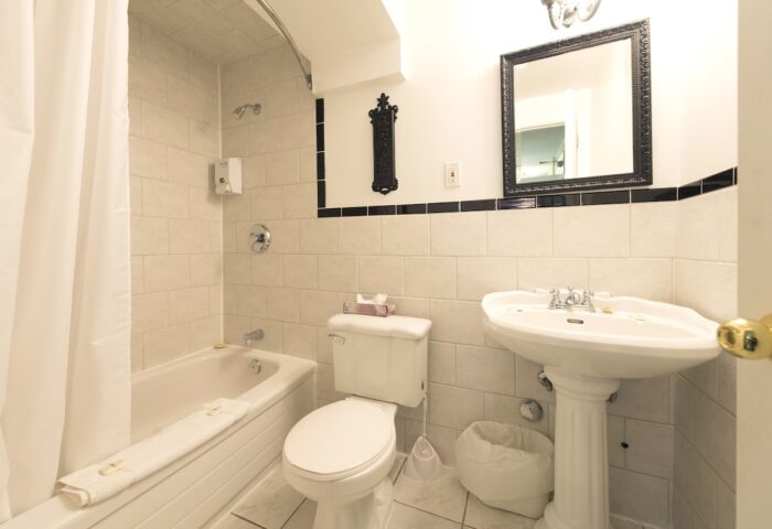Bathroom at Victoria's Mansion Guest House, a gay-friendly hotel. Bathtub, toilet, and sink. Black and white tile. Mirror above sink.