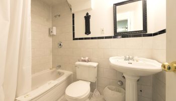 Bathroom at Victoria's Mansion Guest House, a gay-friendly hotel. Bathtub, toilet, and sink. Black and white tile. Mirror above sink.