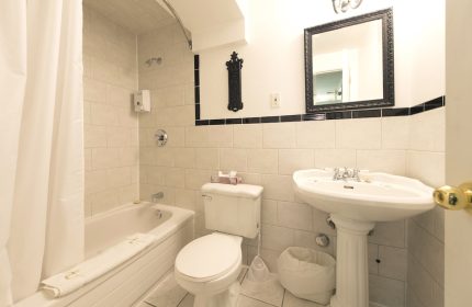 Bathroom at Victoria's Mansion Guest House, a gay-friendly hotel. Bathtub, toilet, and sink. Black and white tile. Mirror above sink.