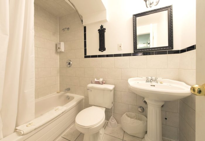 Bathroom at Victoria's Mansion Guest House, a gay-friendly hotel. Bathtub, toilet, and sink. Black and white tile. Mirror above sink.
