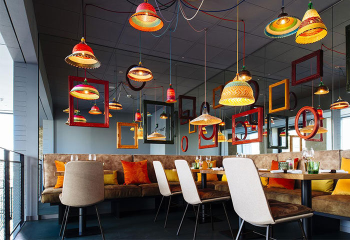 Vienna House Andel’s Berlin restaurant interior. Colorful lamps and frames hang above tables and seating. Gay-friendly hotel, pet-friendly.